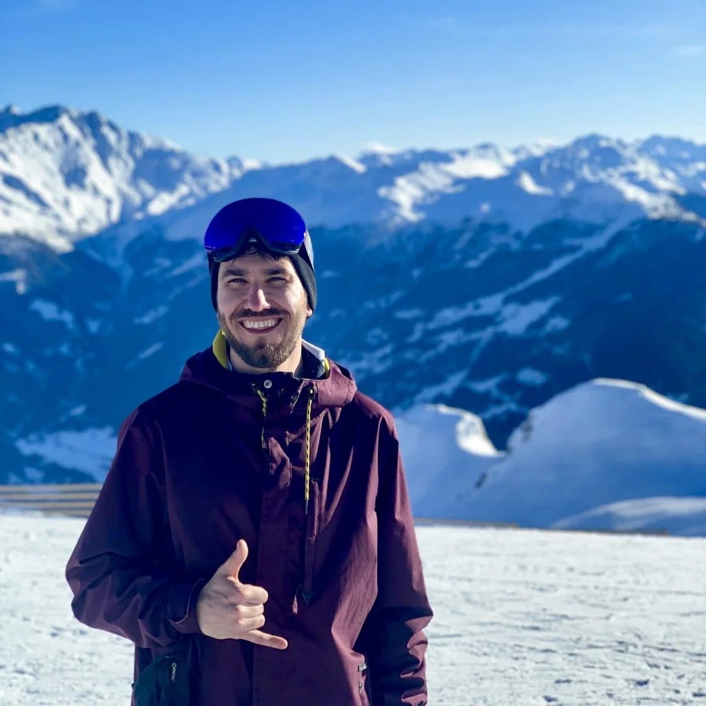 Man (Maciej) standing on a snow field, giving looking and smiling at camera.